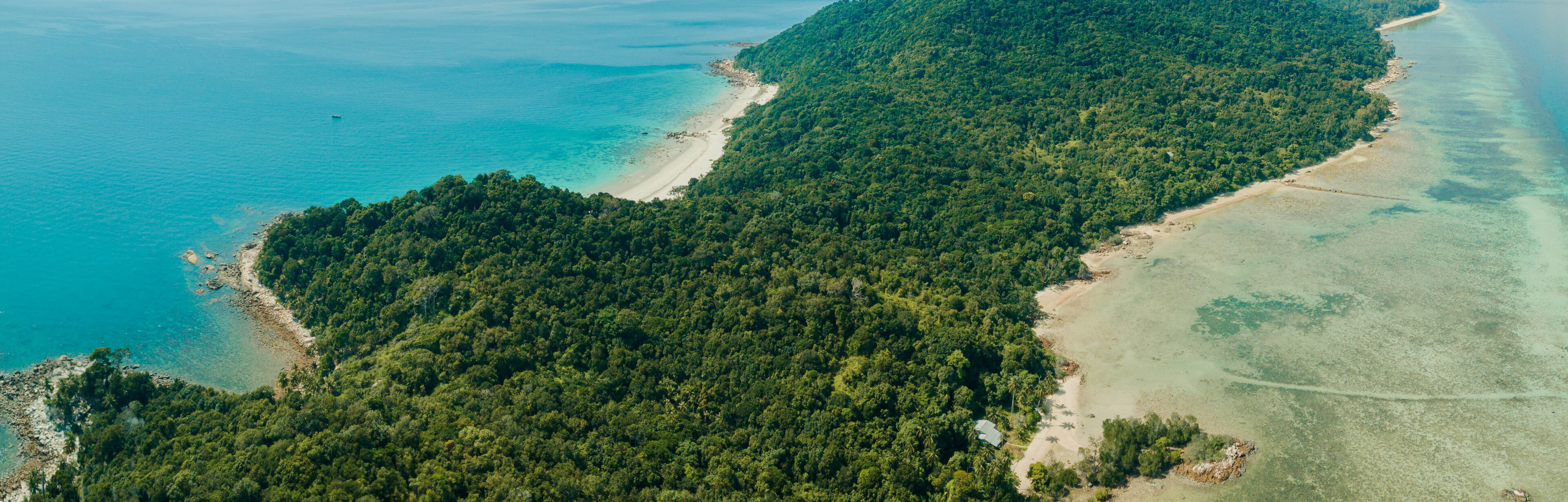An aerial view of a tropical island with dense forest, clear turquoise waters, and sandy beaches.