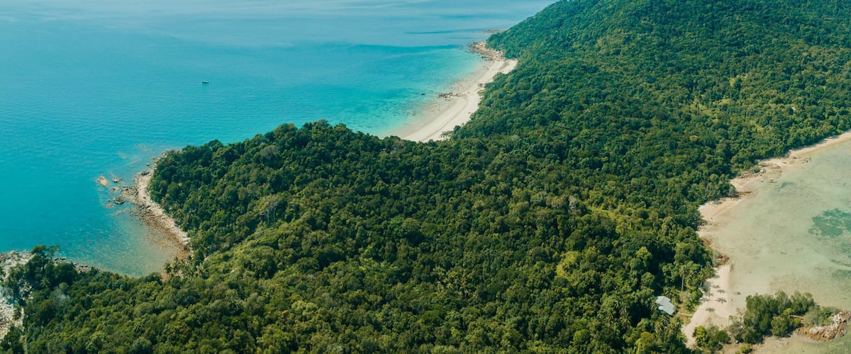 An aerial view of a tropical island with dense forest, clear turquoise waters, and sandy beaches.