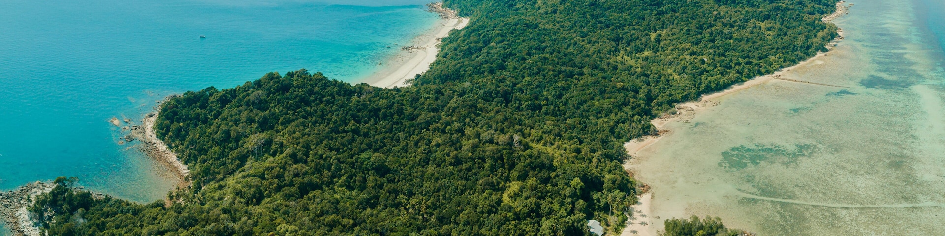 An aerial view of a tropical island with dense forest, clear turquoise waters, and sandy beaches.