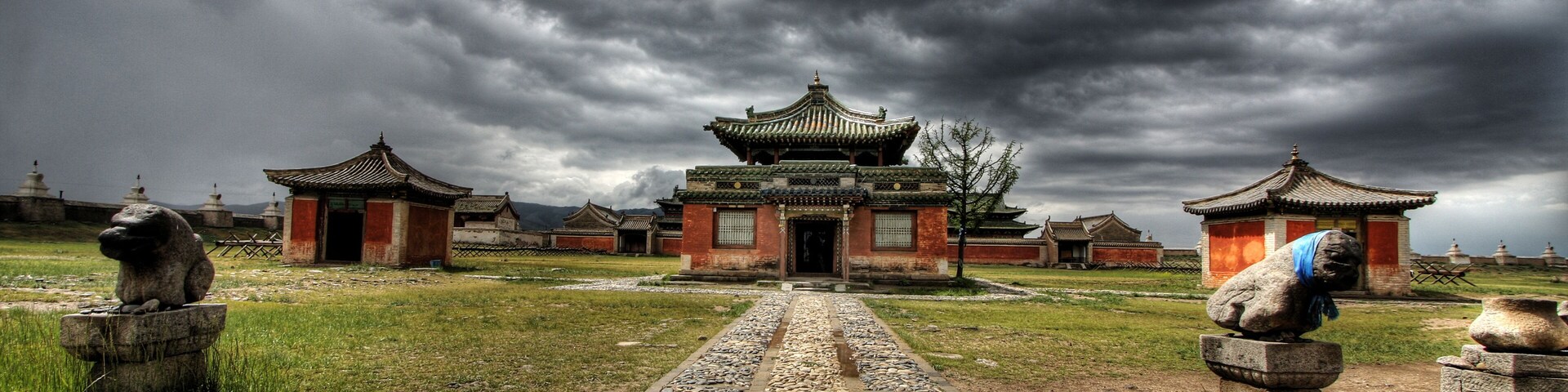 Un complejo de templos chinos tradicionales con una edificación central y dos estructuras más pequeñas a cada lado, rodeado por un camino de piedra y estatuas de leones de piedra.