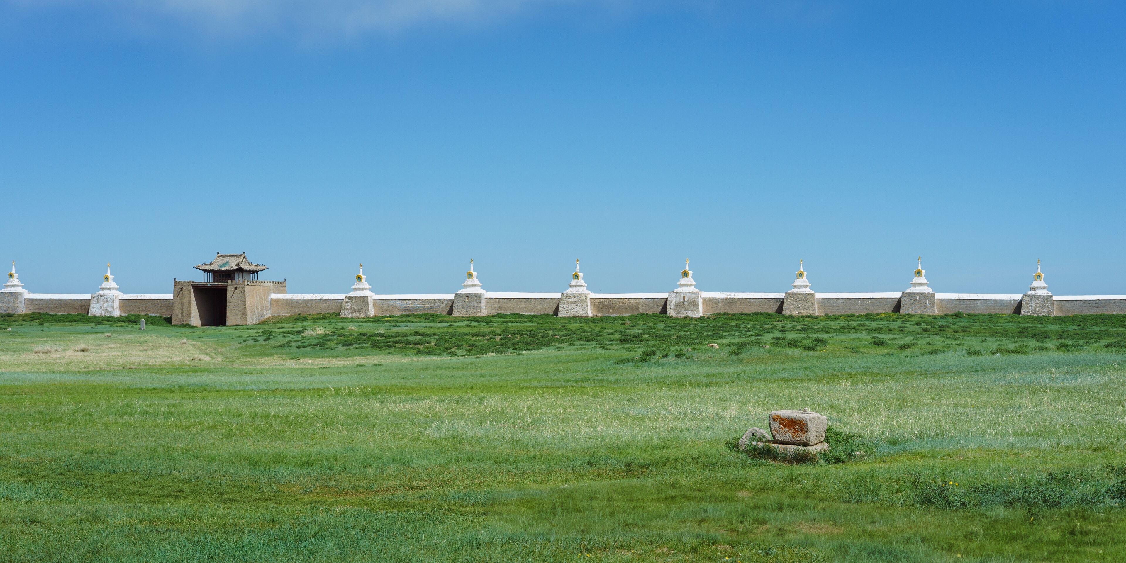 A grassy field with a traditional building and a row of white stupas.