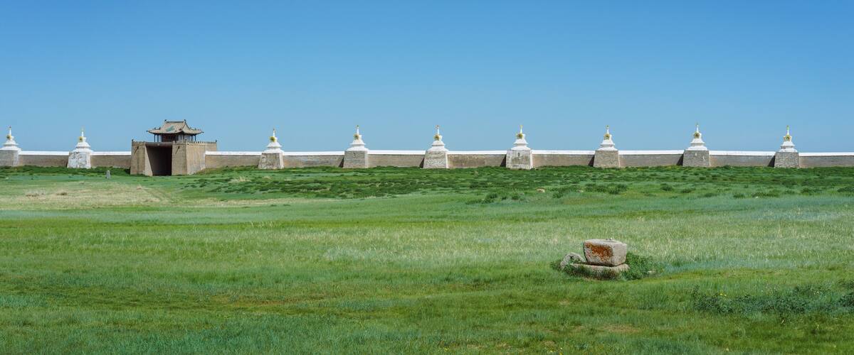 A grassy field with a traditional building and a row of white stupas.