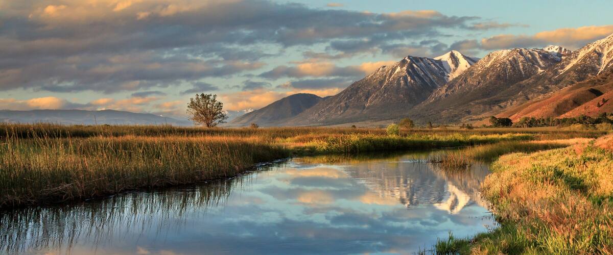 A calm river reflecting the surrounding landscape, with mountains in the background and a clear sky.