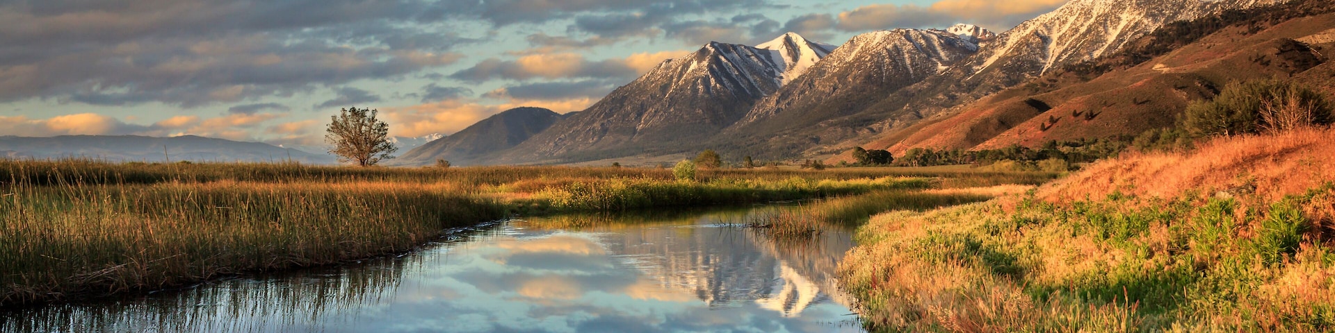 A calm river reflecting the surrounding landscape, with mountains in the background and a clear sky.