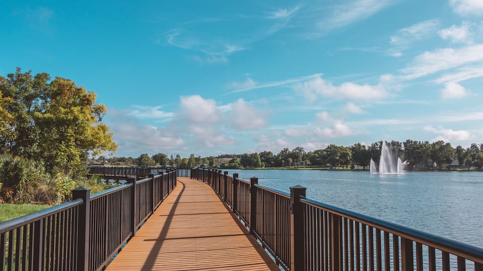 A wooden boardwalk by a lake with a fountain.
