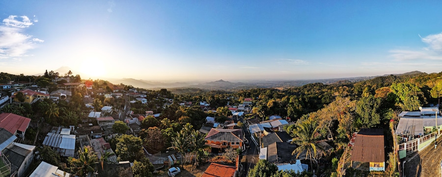 A panoramic view of a town with houses, roads, and a mountain range in the background.