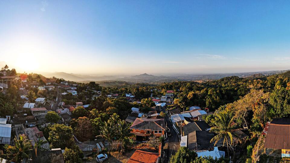A panoramic view of a town with houses, roads, and a mountain range in the background.