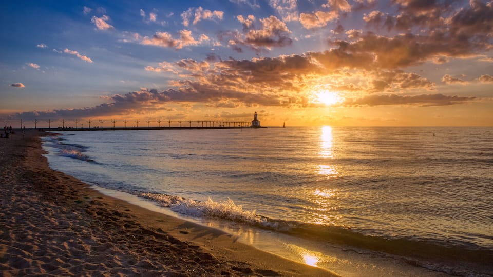A sunset over a beach with a pier extending into the water.