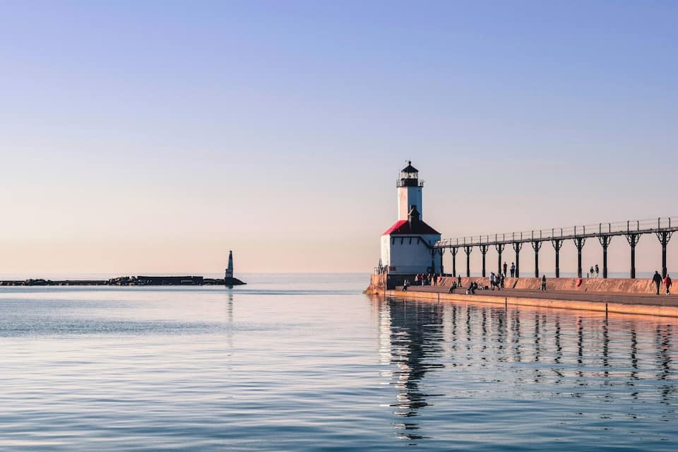 Farol e cais com águas calmas e céu claro.