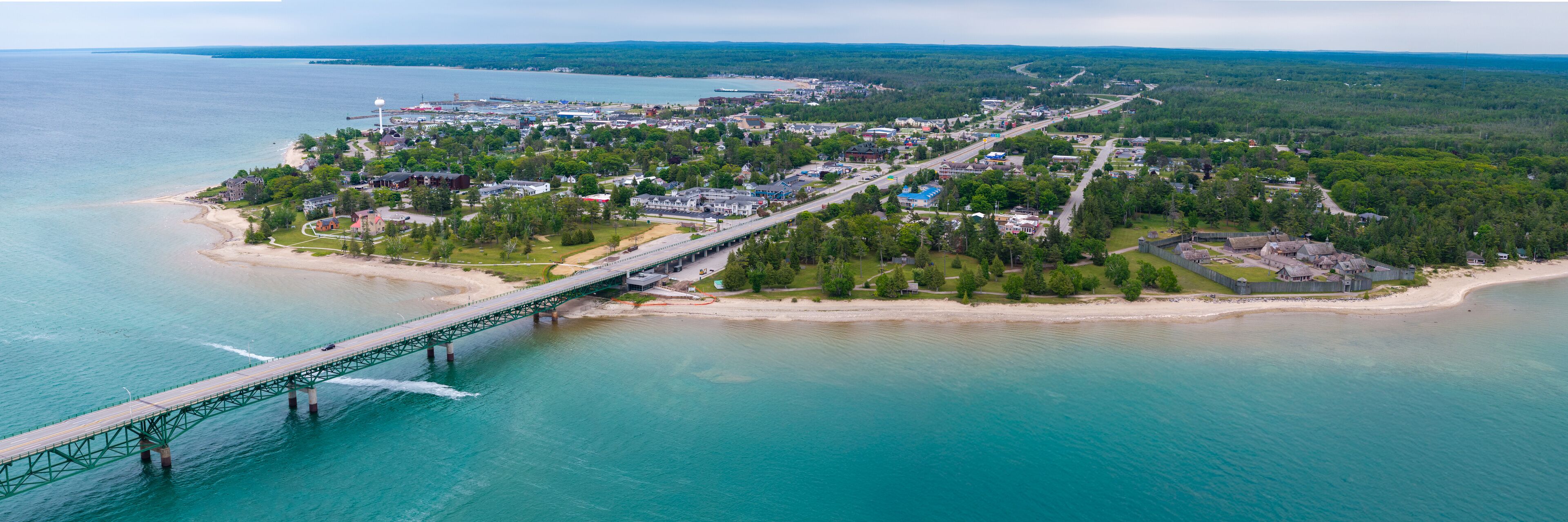 An aerial view of a coastal town with a bridge connecting to a peninsula, surrounded by water and greenery.