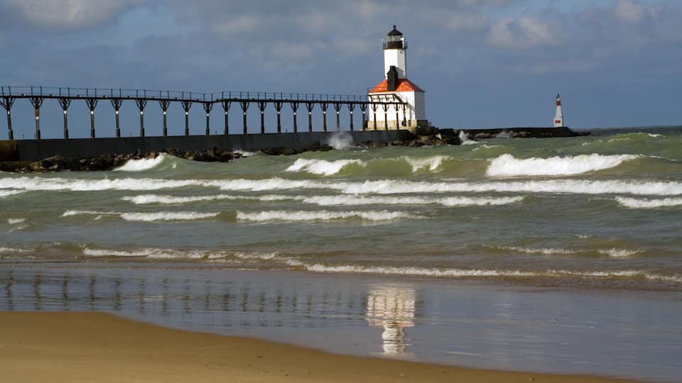 A lighthouse on a pier with waves crashing against it.