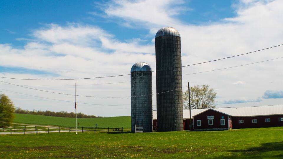 Two large silos, a barn, and a green field under a blue sky.