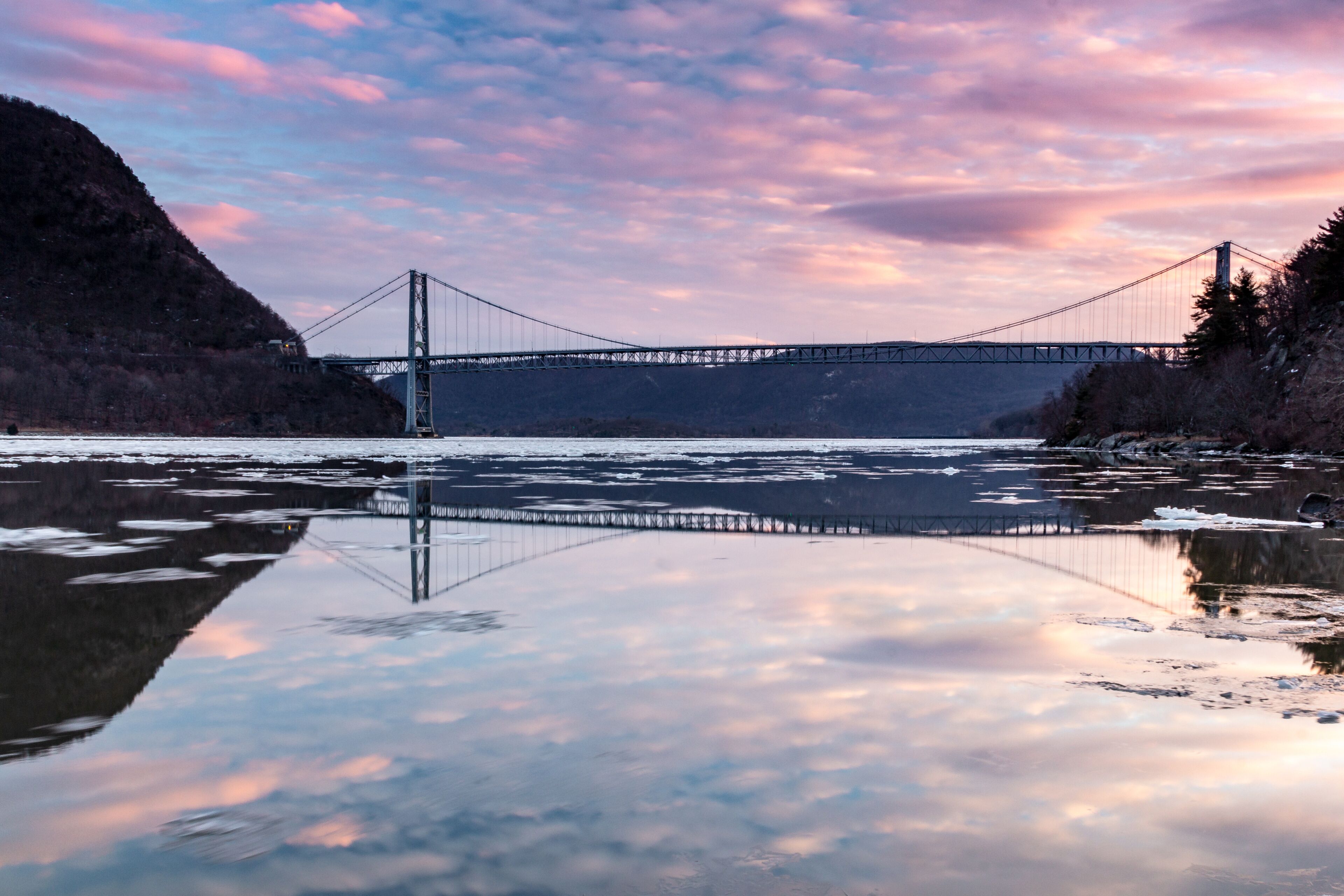 Fort Montgomery, NY / United States - Jan. 26, 2020: A view of the Bear Mountain Bridge at Sunset.  Clouds and bridge reflect in the Hudson River.