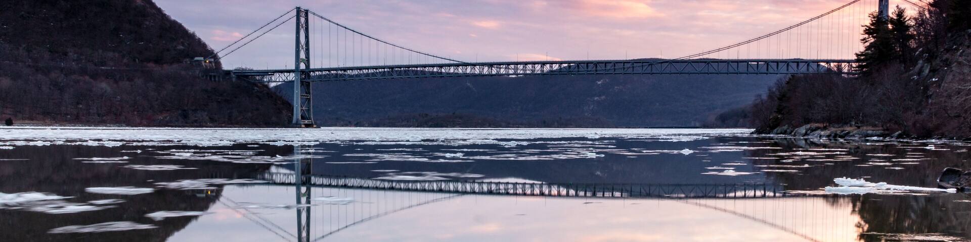 Fort Montgomery, NY / United States - Jan. 26, 2020: A view of the Bear Mountain Bridge at Sunset. Clouds and bridge reflect in the Hudson River.