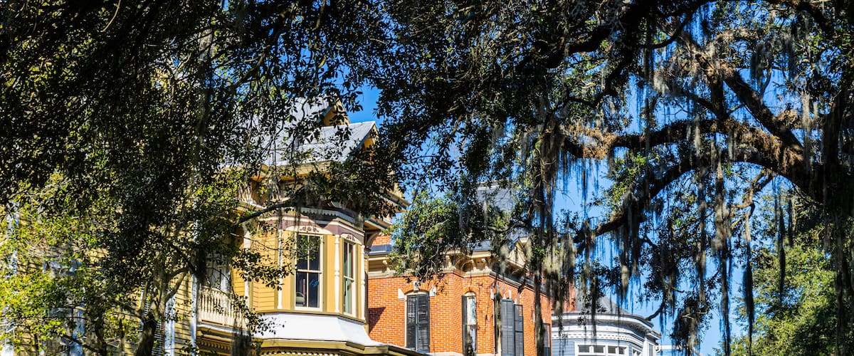 A row of historic brick houses with distinctive architectural features, surrounded by lush greenery and trees with Spanish moss.