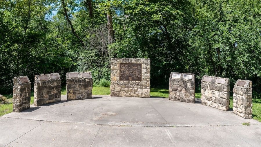 A stone monument with inscriptions, surrounded by a paved area and dense green trees.