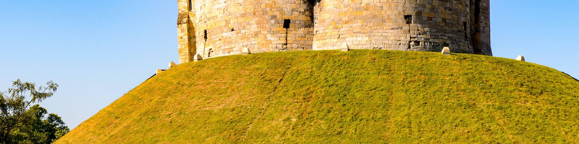 A historic stone tower on a grassy hill under a clear blue sky.