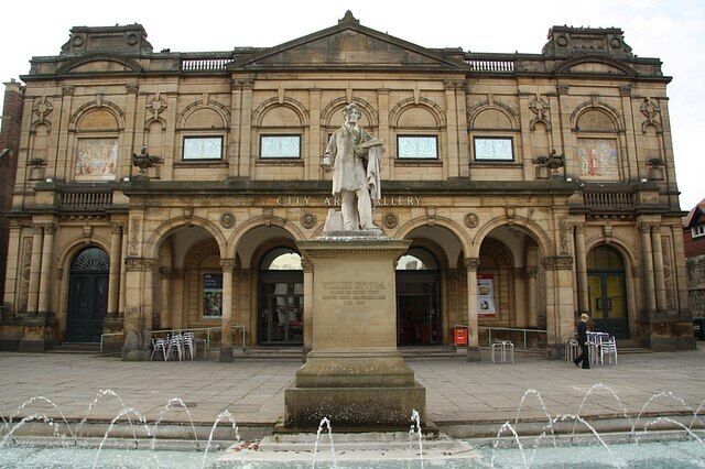 A historic building with a statue in front, arched doorways, and a fountain.