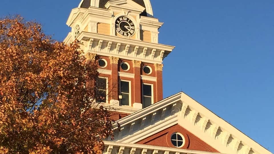 A clock tower with a dome and a clock face, surrounded by autumn-colored trees.