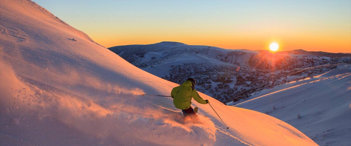 A skier on a snowy slope during sunset.