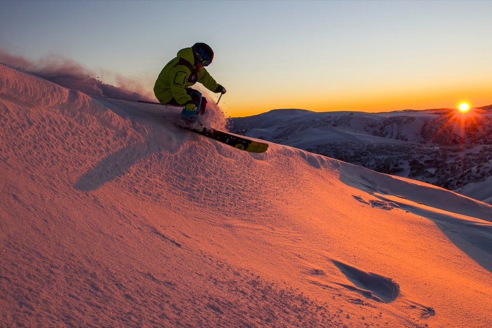 A skier in a yellow jacket descending a snow-covered slope during sunset.