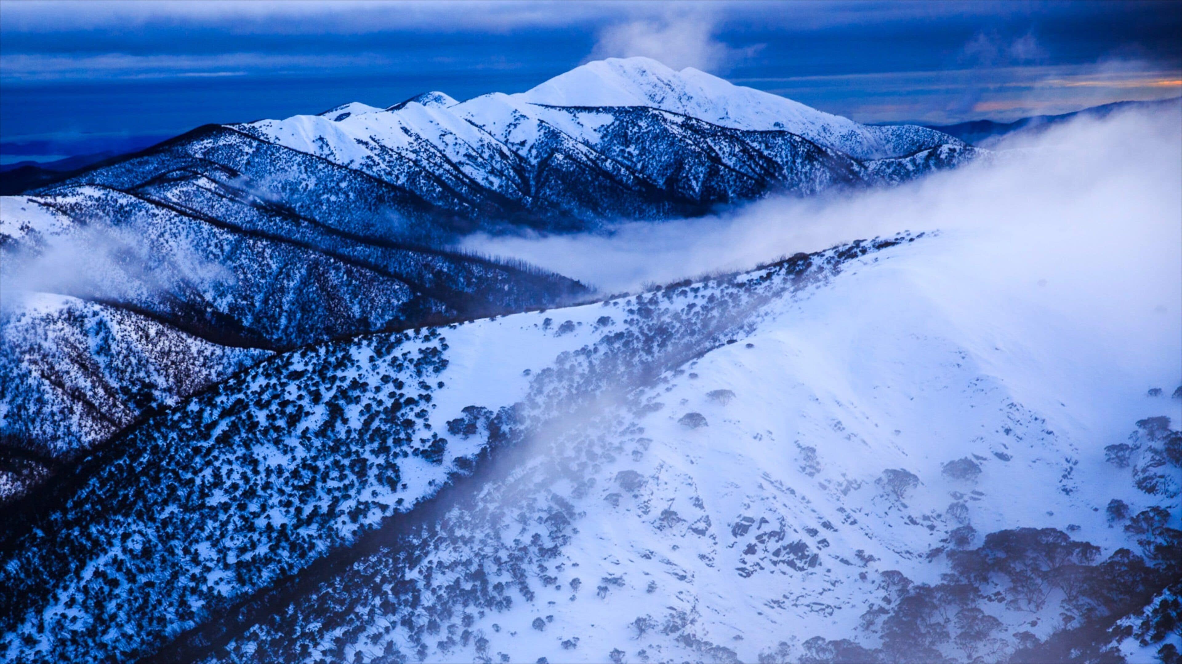 A snow-covered mountain range with a valley and mist.