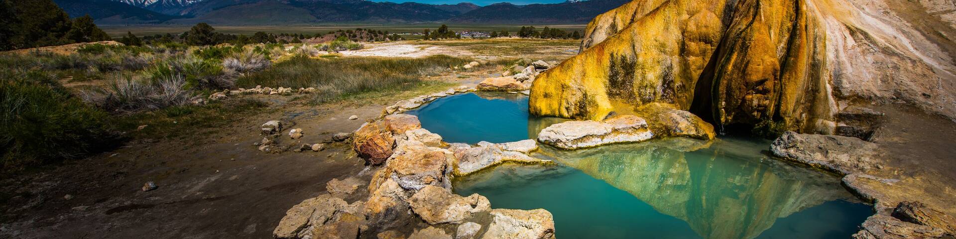 A geothermal hot spring with mineral deposits, surrounded by a mountainous landscape.