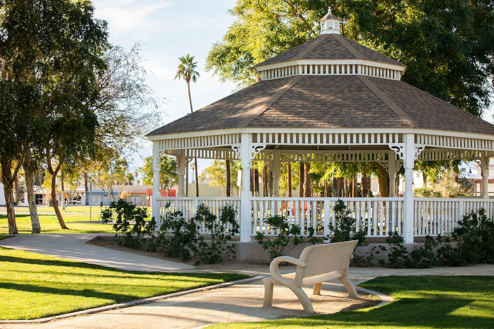 A gazebo with a white fence and a bench in a park.