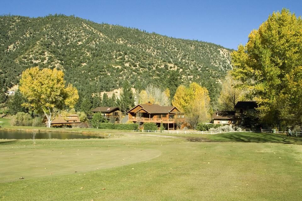 A golf course with a clubhouse, a pond, and a mountainous backdrop.