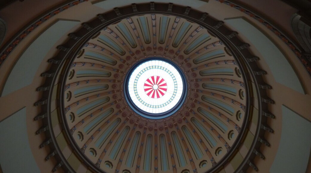 The Rotunda is one of the most remarkable spaces in the Statehouse. Stretching 120 feet from the floor to the oculus.
The crown jewel in the Rotunda's dome is its 29-foot-wide skylight. The center circle of the skylight is a hand-painted Great Seal of Ohio, a reproduction of the Seal that was in use in 1861 when the Rotunda was completed.
The seal in the dome, which is 3ft in diameter, is slightly different than the seal in use today. This seal not only has the mountains, a sheaf of wheat and a bundle of arrows, but it also includes a canal boat in the foreground. The canals were an important mode of transportation at the time this seal was designed (circa 1847). The seal has changed five times in the course of Ohio's history.
#architecture