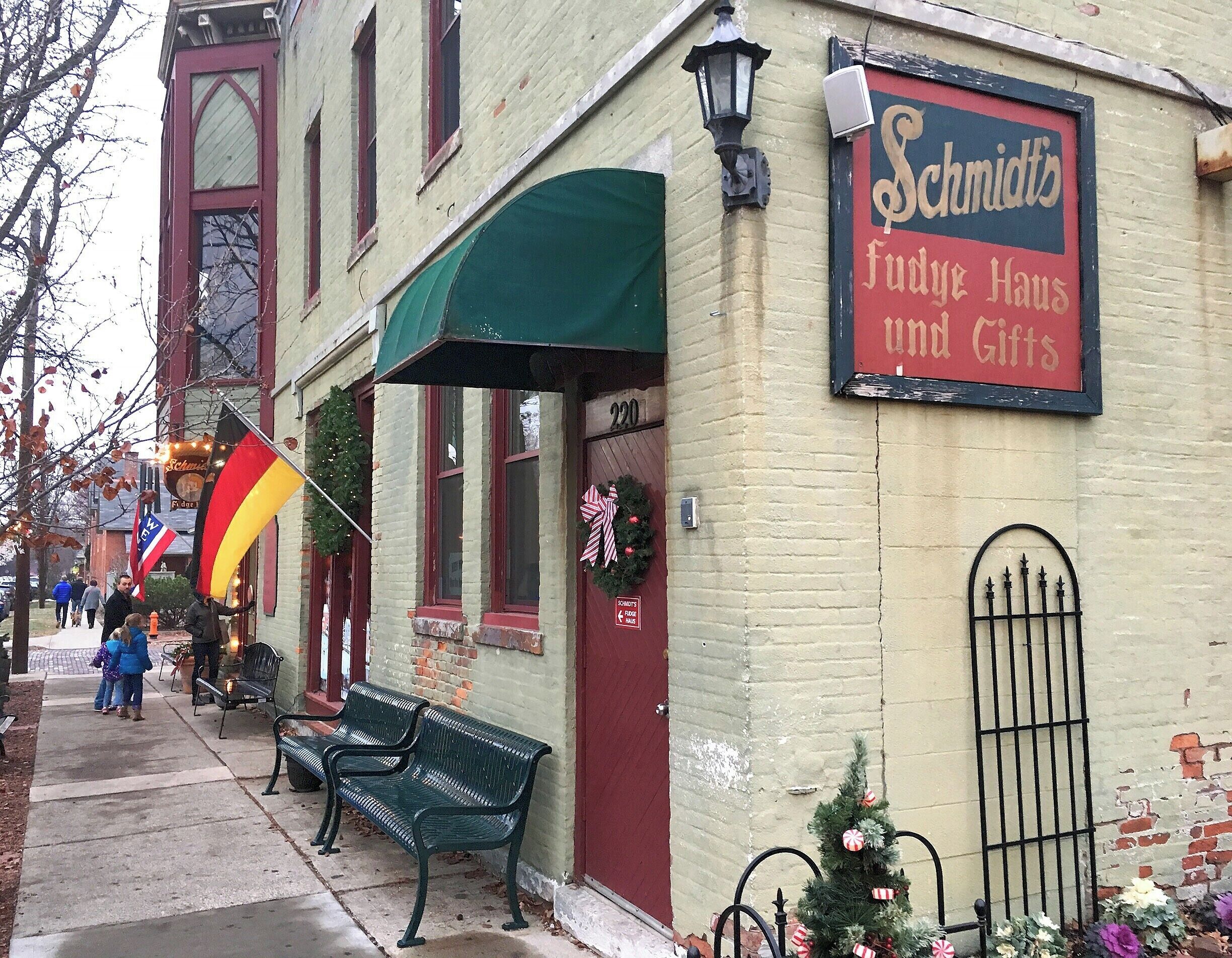 A building with a sign reading "Schmidts Fudge Haus und Gifts" and a Christmas tree decorated with candy canes.