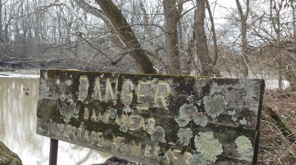 An old wooden sign warning about the lowhead dam just down stream. There are newer looking metal signs. The lichen encrusted sign reads "Danger, Dam Ahead. Portage at Marker". This can be found east of Antrim lake on the western shore of the river, along the trails that snake through the wooded area of the park. #urbanjungle