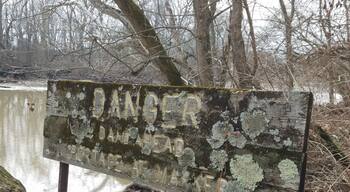 An old wooden sign warning about the lowhead dam just down stream. There are newer looking metal signs. The lichen encrusted sign reads "Danger, Dam Ahead. Portage at Marker". This can be found east of Antrim lake on the western shore of the river, along the trails that snake through the wooded area of the park. #urbanjungle