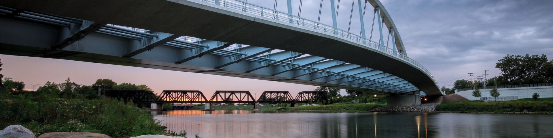 Uma ponte moderna sobre um rio calmo, sob um céu nublado.