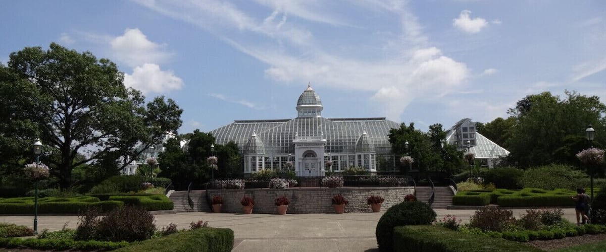 The John F. Wolfe Palm House at the Franklin Park Conservatory basking beneath blue skies and jet trails The palm house opened to the public in 1895.