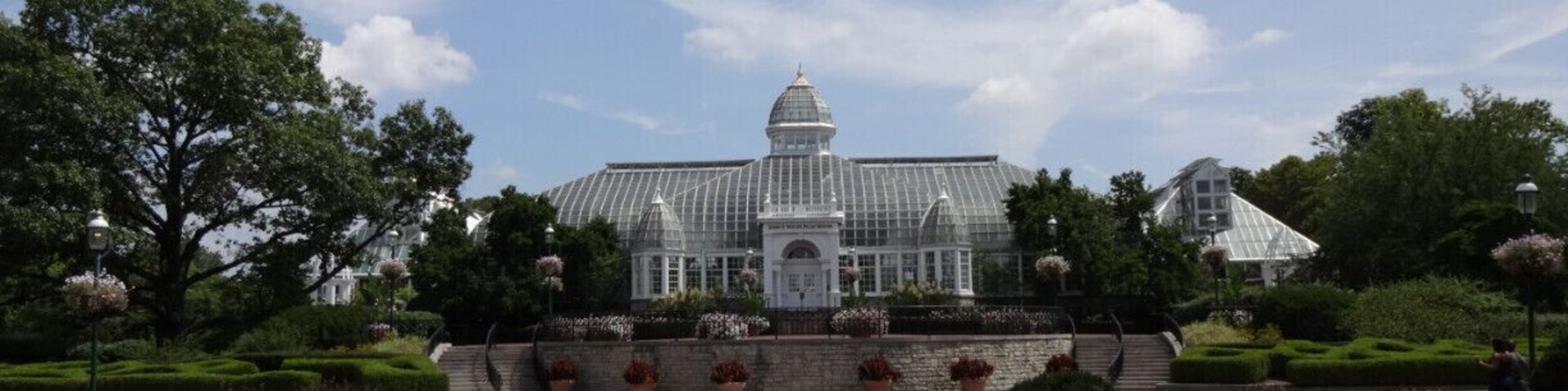 The John F. Wolfe Palm House at the Franklin Park Conservatory basking beneath blue skies and jet trails The palm house opened to the public in 1895.