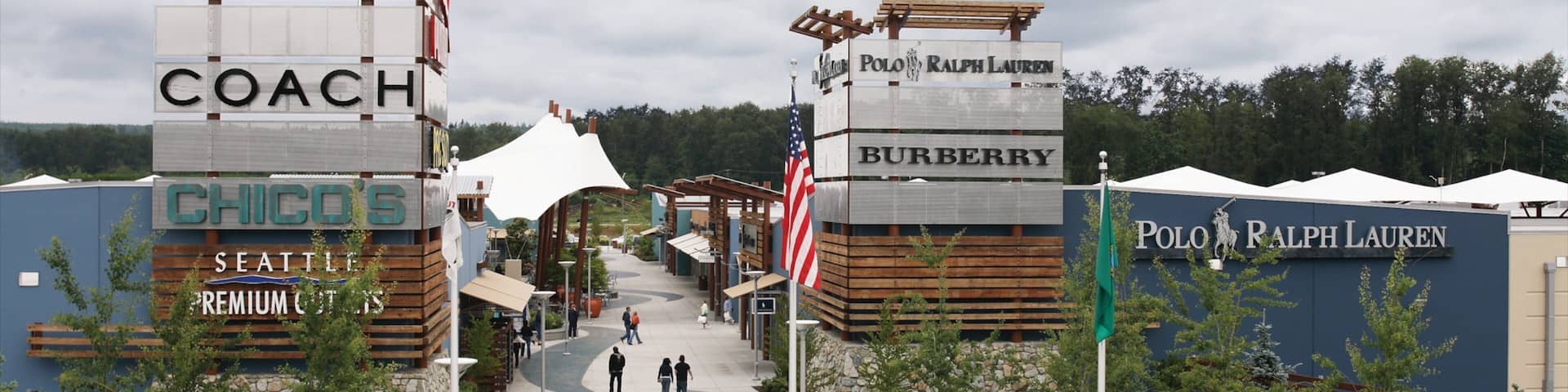 A shopping area with signs for Calvin Klein Coach, Chicos, Seattle Premium Outlet, Polo Ralph Lauren, and Burberry.