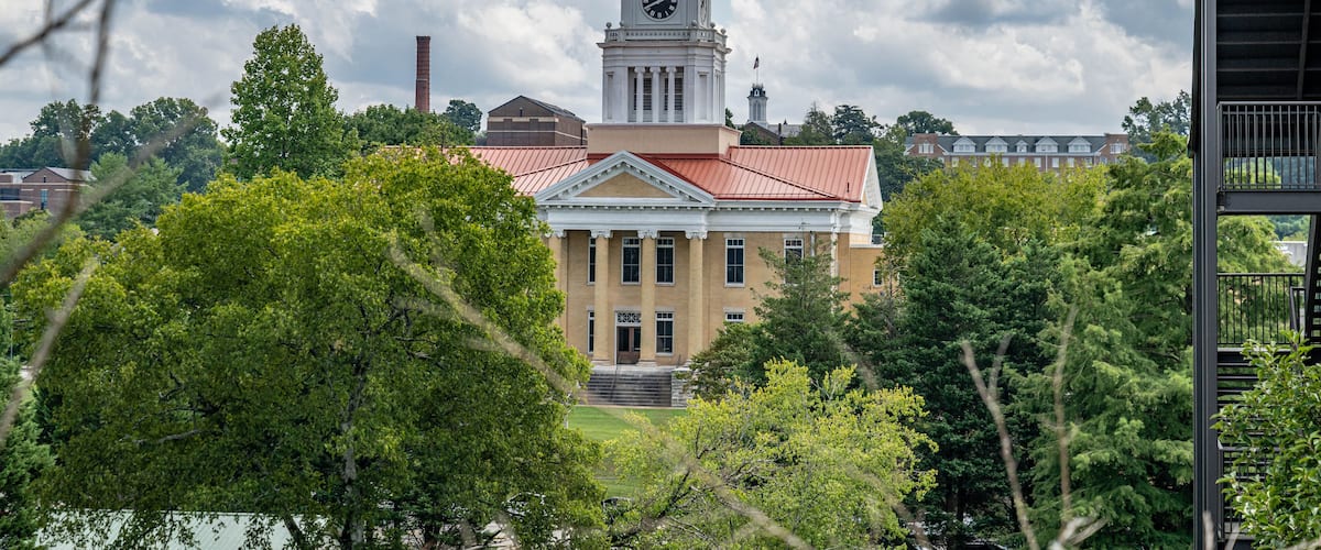 A historic building with a clock tower, surrounded by lush greenery and a partly cloudy sky.