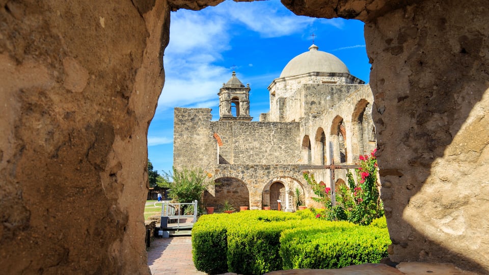 An ancient stone building with a bell tower and dome, viewed through a stone archway.