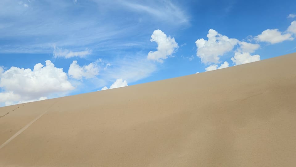 A sand dune under a clear blue sky with scattered clouds.