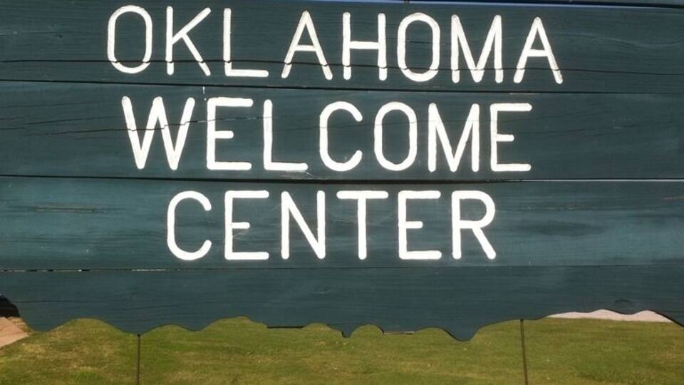 A wooden sign with "Oklahoma Welcome Center" and "Gift Shop" written on it.