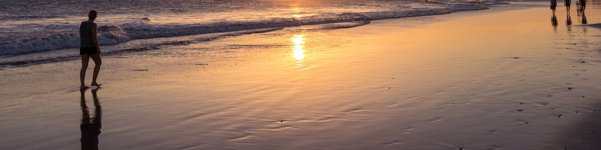 A beach at sunset with a person standing and waves crashing onto the shore.