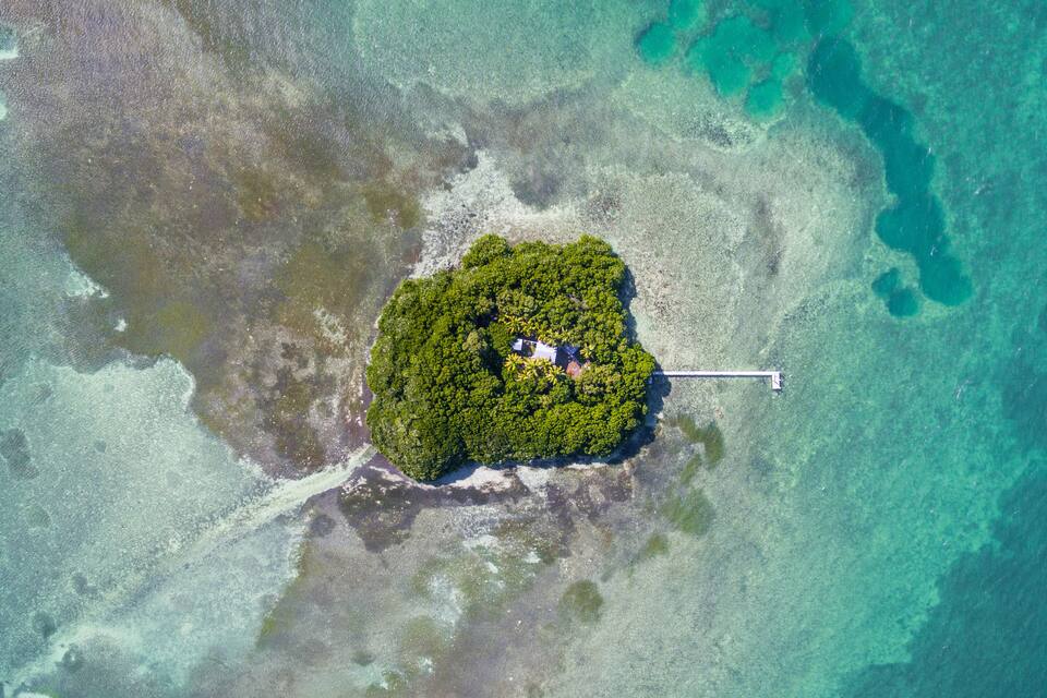 An aerial view of a small, lush island with dense vegetation and a dock extending into the turquoise waters.