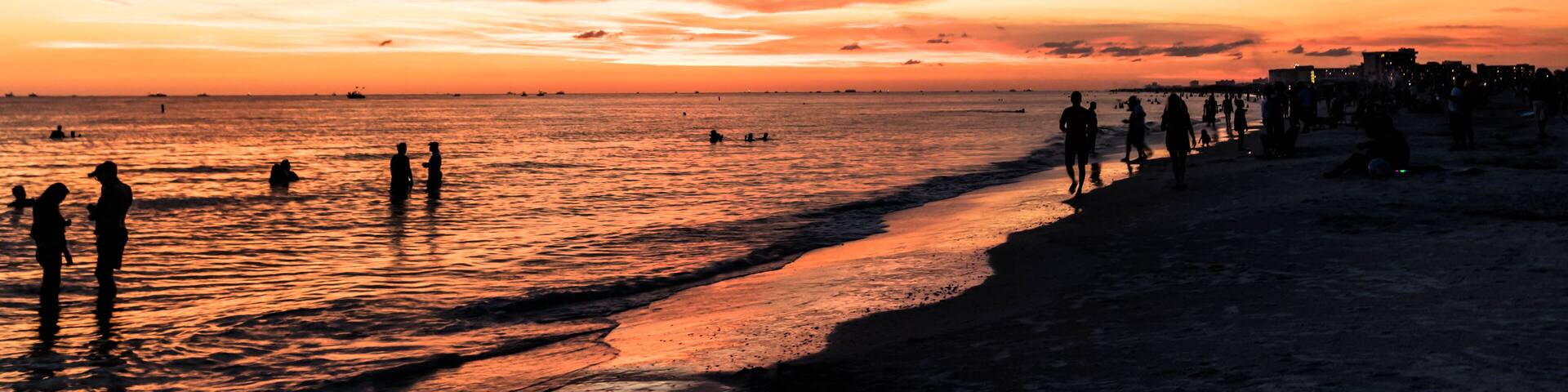 Une plage au coucher du soleil, avec les silhouettes de personnes et un frisbee rose sur le sable.