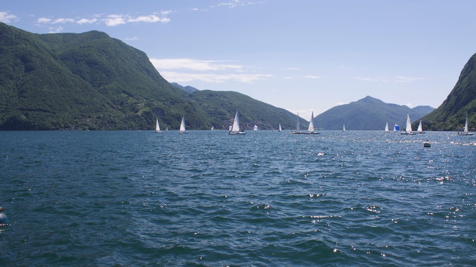 A lake with sailboats and green mountains in the background.