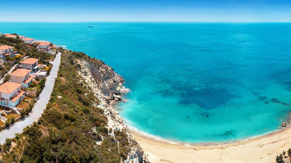Breathtaking aerial panorama of secluded beach, showcasing crystal clear turquoise waters, a picturesque coastline, and charming coastal architecture