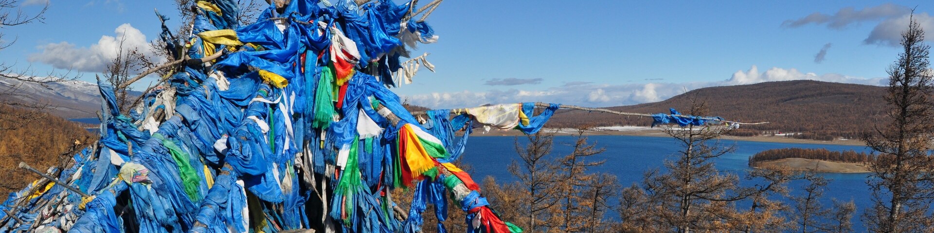 Um colorido conjunto de orações em uma colina rochosa, com um lago e montanhas ao fundo.