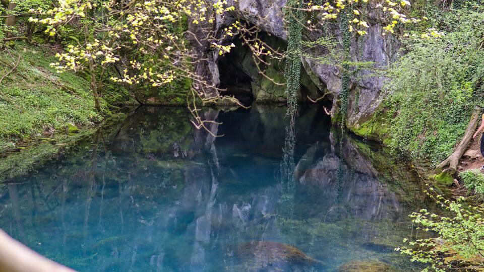 A clear, natural pool surrounded by lush greenery and rocky terrain.