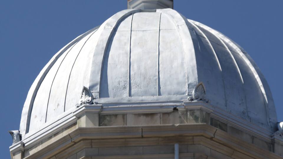 A golden statue of Lady Justice atop a white dome with a clear blue sky in the background.