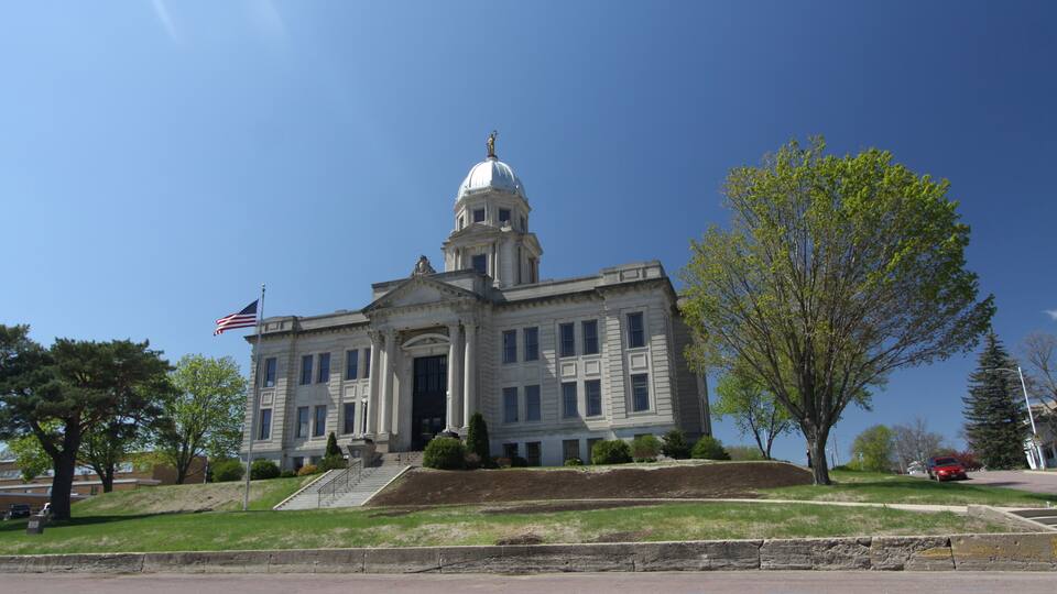A large, historic building with a dome and columns, an American flag, and a well-maintained lawn.
